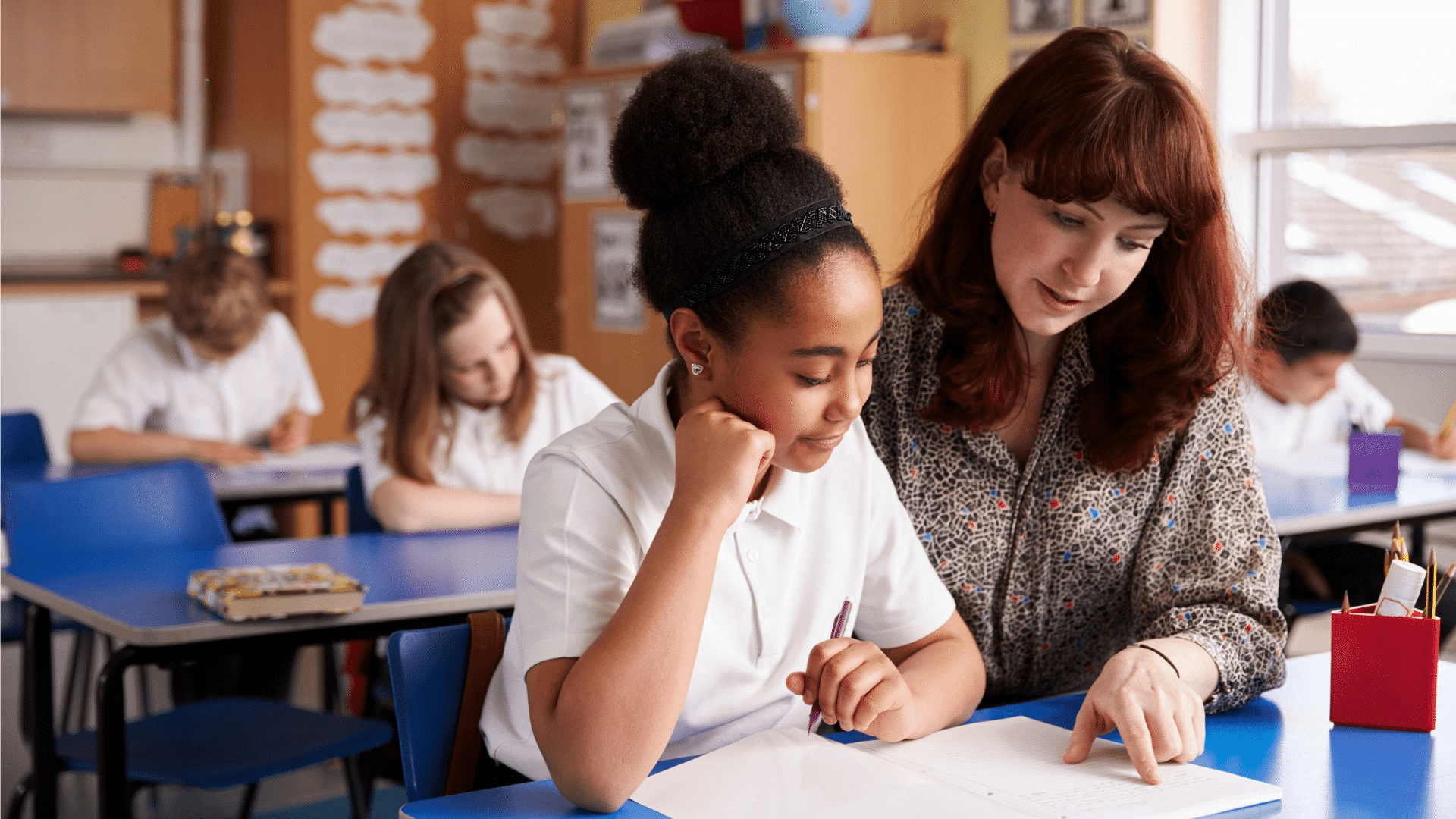 KS2 pupil sat working with red haired teacher